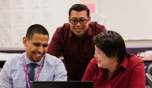 Three teachers gathered together around a computer smiling